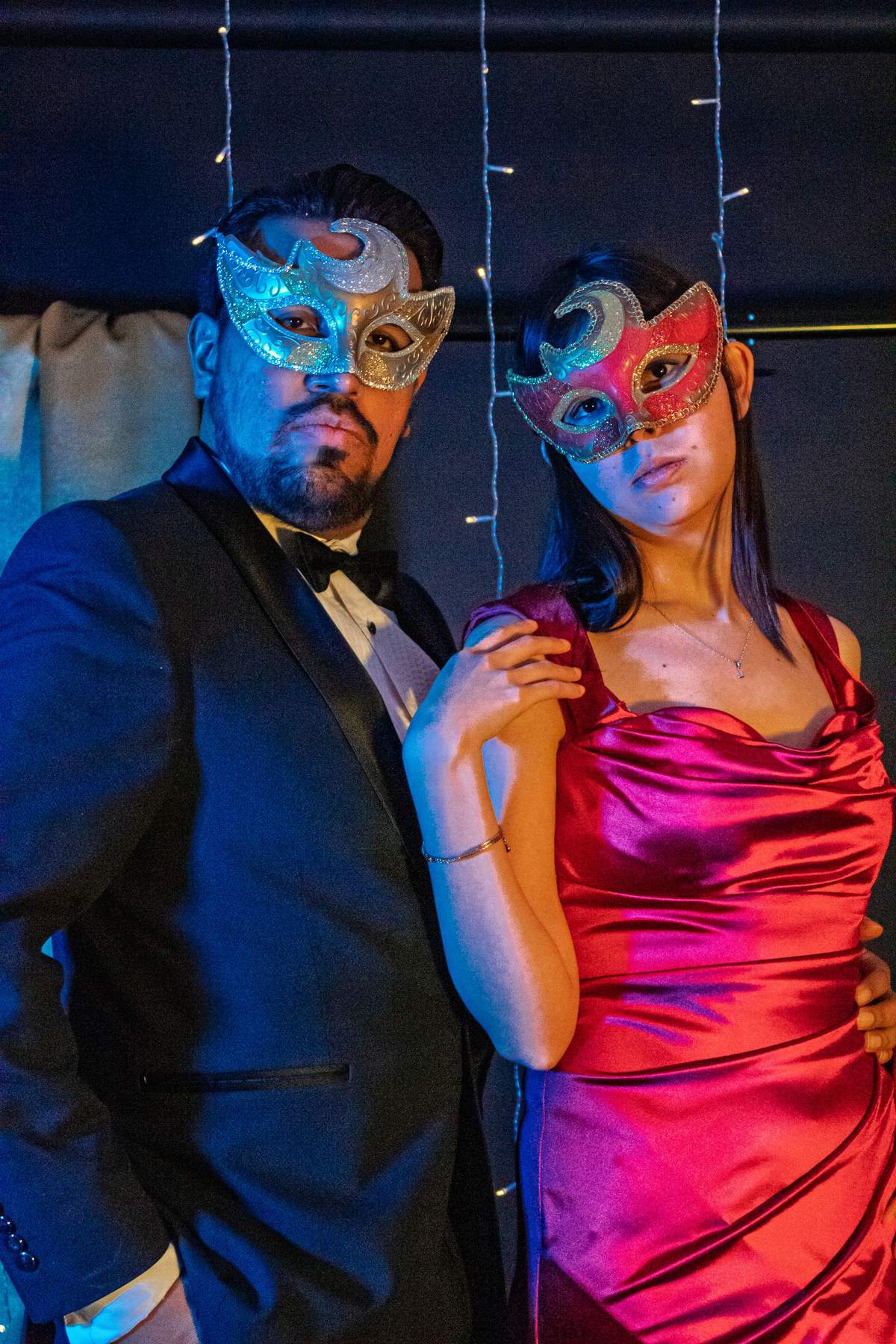 A couple in a tuxedo and a satin evening dress, both wearing glittering masquerade masks