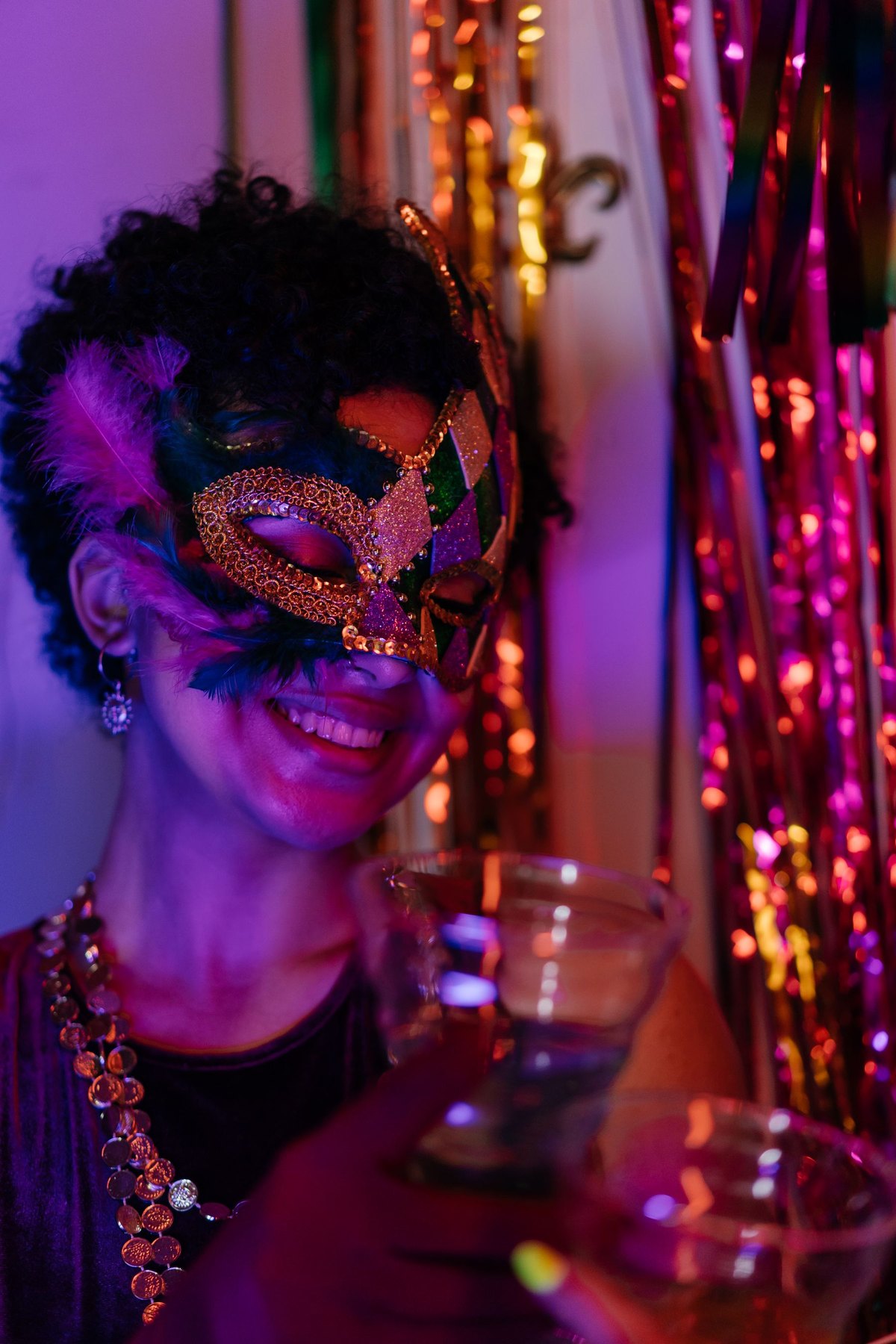 A smiling woman in a gold masquerade mask holding a drink at a party