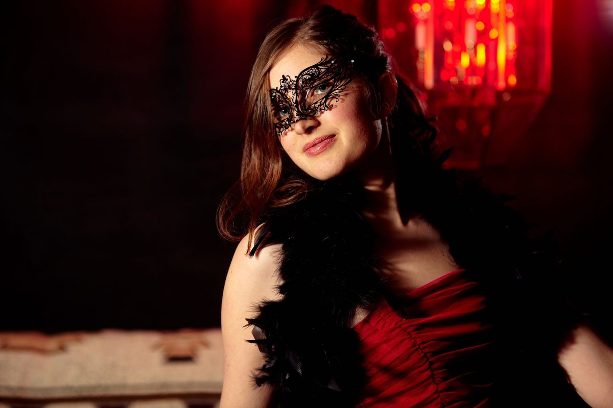 A woman in a red evening dress and black lace mask under low red light